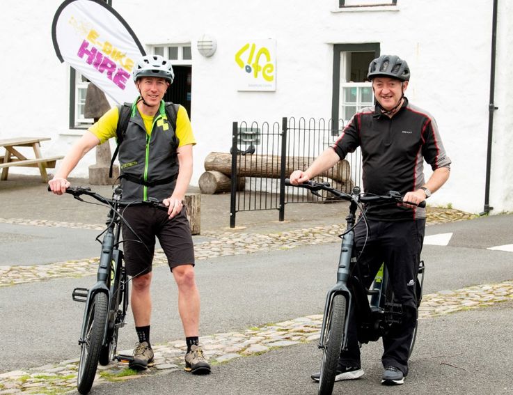 Two men with bicycles, smiling at the camera.