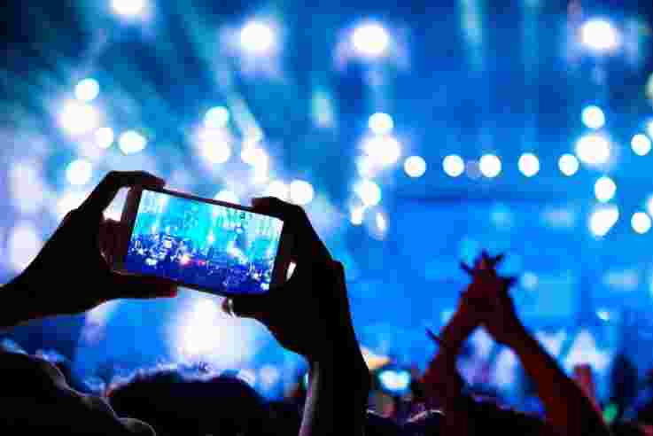 Man taking a video of the show at the concert hall using a smartphone