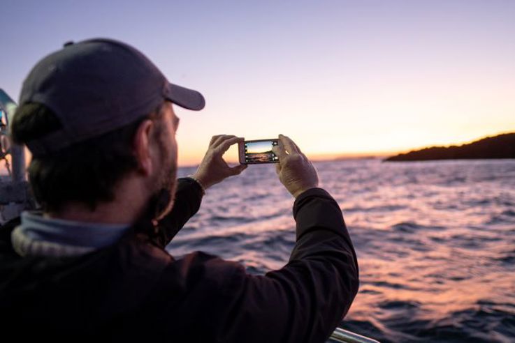 Visitor taking photograph of sunrise while on Catch and Sea Food Tour, Portush