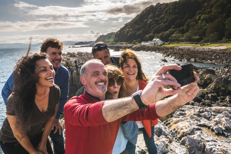 Friends taking photographs together during Causeway's Toast the Coast food tour, as part of the Embrace a Giant Spirit experience.