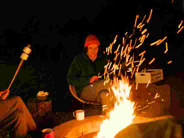 Friends toasting marshmallows around campfire
