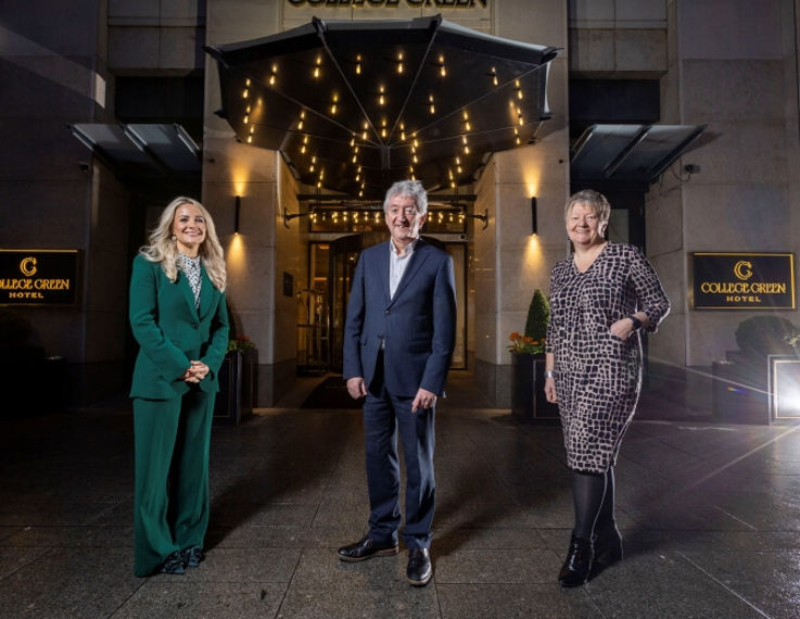 Three individuals standing outside the entrance of the College Green Hotel, smiling at the camera.