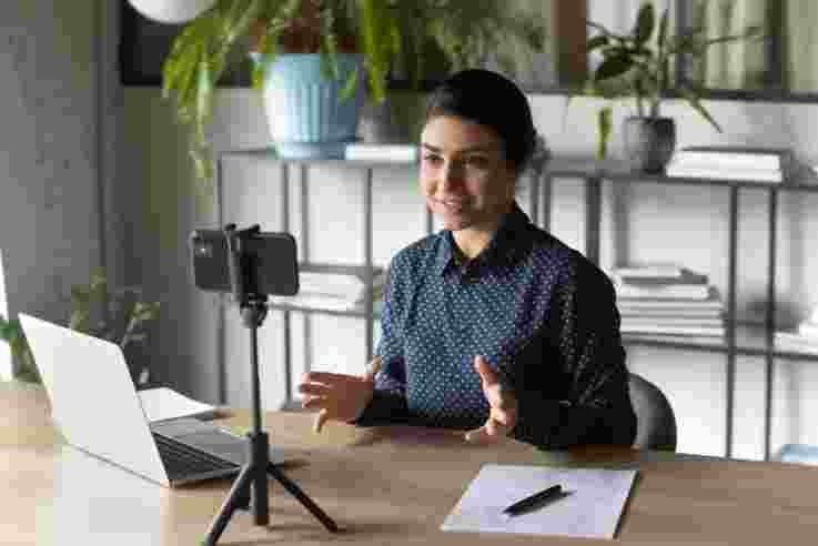 businesswoman recording webinar, using smartphone on tripod, sitting at desk in office